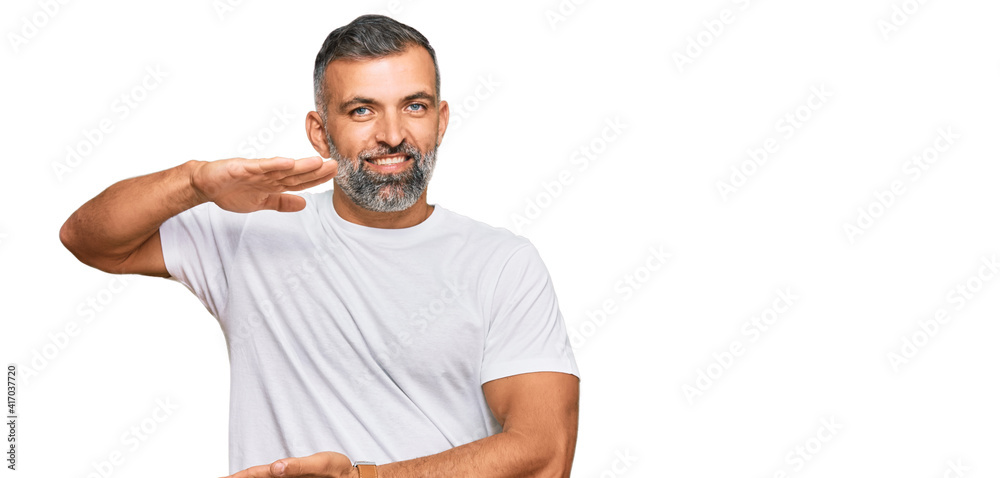 Middle age handsome man wearing casual white tshirt gesturing with hands showing big and large size sign, measure symbol. smiling looking at the camera. measuring concept.