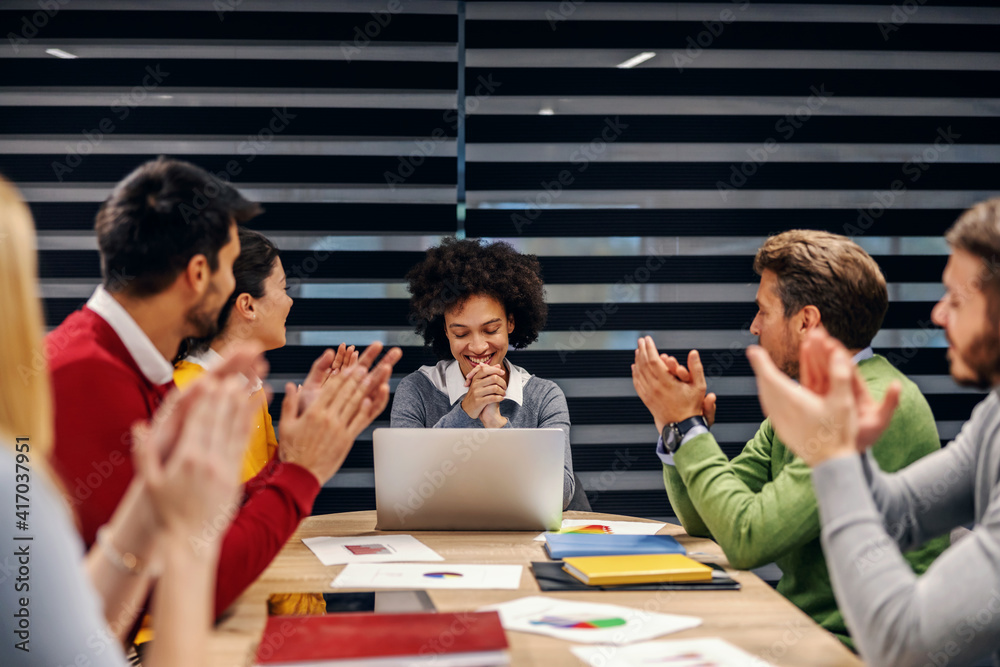 Fototapeta premium Successful mixed race businesswoman sitting in boardroom with her colleagues on meeting. Colleagues clapping for an excellent idea.