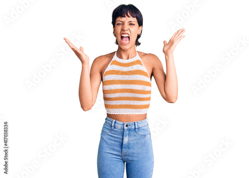 Young brunette woman with short hair wearing casual clothes celebrating mad and crazy for success with arms raised and closed eyes screaming excited. winner concept