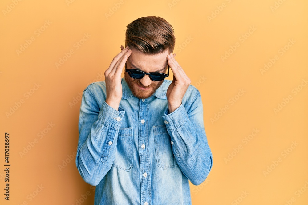 Young redhead man wearing stylish sunglasses suffering from headache desperate and stressed because pain and migraine. hands on head. Young redhead man wearing stylish sunglasses suffering from headache desperate and stressed because pain and migraine. hands on head.