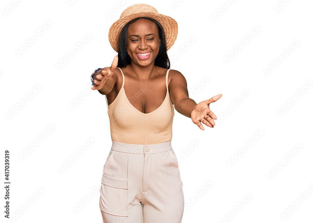 Young black woman wearing summer hat looking at the camera smiling with open arms for hug. cheerful expression embracing happiness. Young black woman wearing summer hat looking at the camera smiling with open arms for hug. cheerful expression embracing happiness.