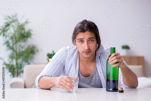 Young male alcoholic drinking whiskey at home