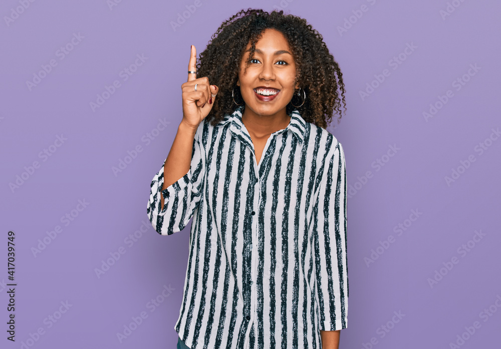 Young african american girl wearing casual clothes pointing finger up with successful idea. exited and happy. number one. Young african american girl wearing casual clothes pointing finger up with successful idea. exited and happy. number one.