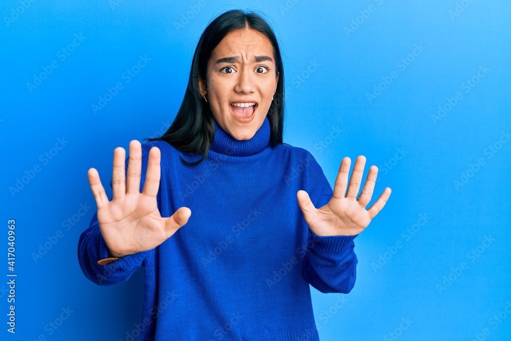 Young asian woman wearing casual winter sweater afraid and terrified with fear expression stop gesture with hands, shouting in shock. panic concept. Young asian woman wearing casual winter sweater afraid and terrified with fear expression stop gesture with hands, shouting in shock. panic concept.