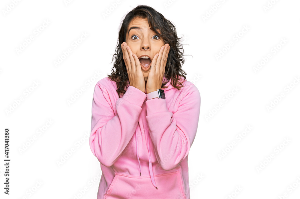 Young hispanic woman wearing casual sweatshirt afraid and shocked, surprise and amazed expression with hands on face Young hispanic woman wearing casual sweatshirt afraid and shocked, surprise and amazed expression with hands on face