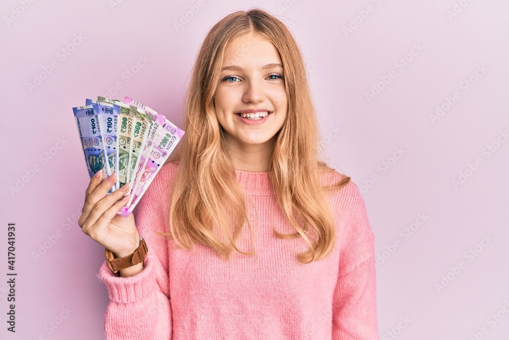 Beautiful young caucasian girl holding indian rupee banknotes looking positive and happy standing and smiling with a confident smile showing teeth Beautiful young caucasian girl holding indian rupee banknotes looking positive and happy standing and smiling with a confident smile showing teeth