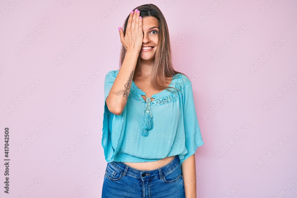 Beautiful caucasian woman wearing casual clothes covering one eye with hand, confident smile on face and surprise emotion. Beautiful caucasian woman wearing casual clothes covering one eye with hand, confident smile on face and surprise emotion.