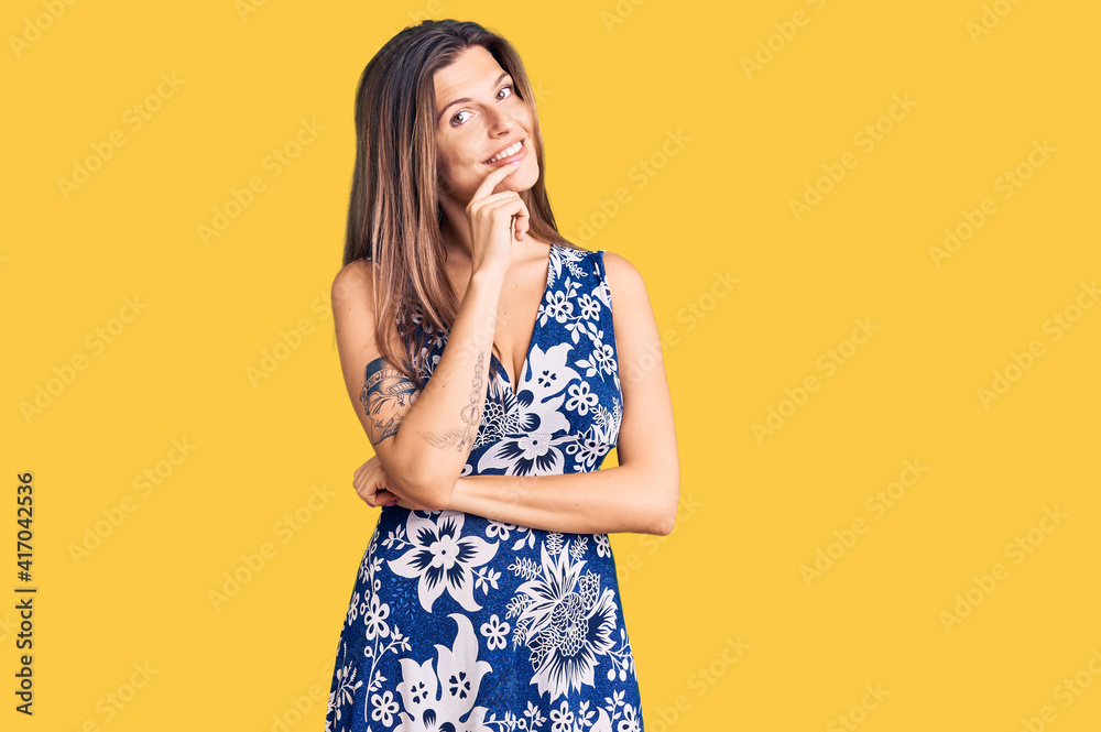 Beautiful caucasian woman wearing summer dress looking confident at the camera with smile with crossed arms and hand raised on chin. thinking positive. Beautiful caucasian woman wearing summer dress looking confident at the camera with smile with crossed arms and hand raised on chin. thinking positive.