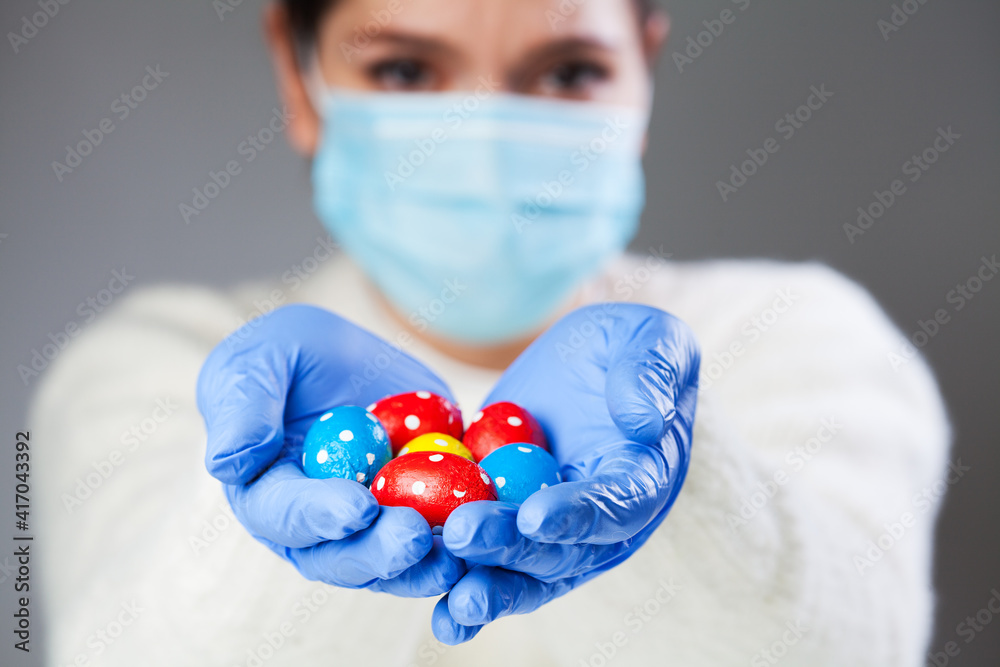 Person wearing face mask and blue protective medical gloves holding chocolate Easter eggs Person wearing face mask and blue protective medical gloves holding chocolate Easter eggs