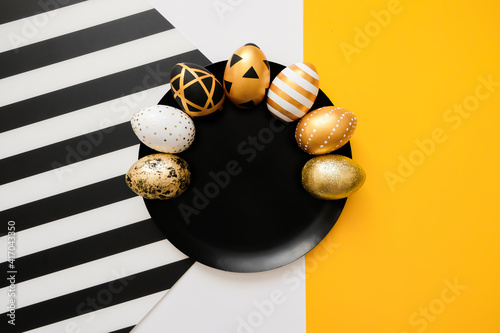 Stylish background with Easter golden decorated eggs on black plate. Trendy flat lay easter concept. Happy Easter card with copy space for text. Minimal easter concept. Striped and yellow background