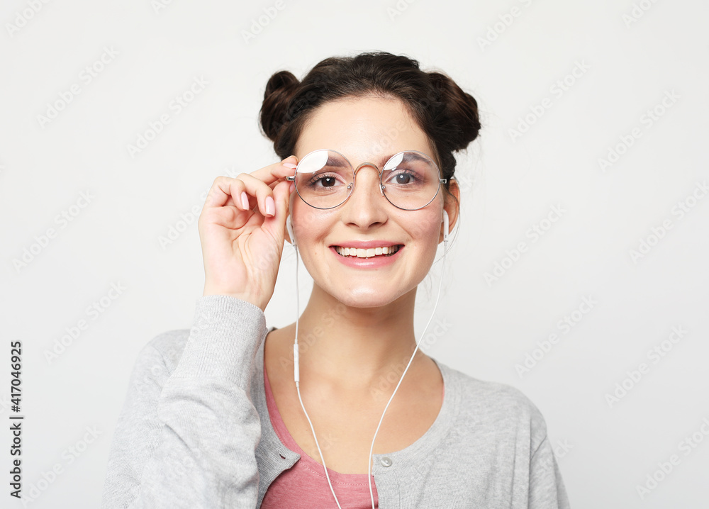 Young brunette woman girl wearing glasses isolated on light grey wall background studio portait. People lifestyle concept. Listen music with headphones.