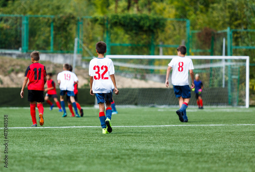Young sport boys in white and red sportswear running and kicking a ball on pitch. Soccer youth team plays football in summer. Activities for kids, training 
