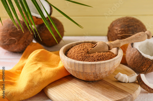 Bowl of sugar and sweet coconuts on light wooden background