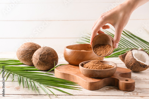 female hand and sweet coconut sugar on light wooden background