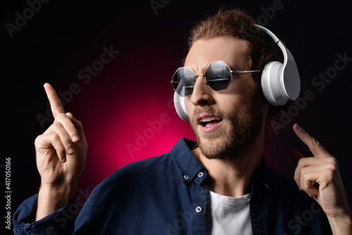 Handsome young man listening to music on dark background