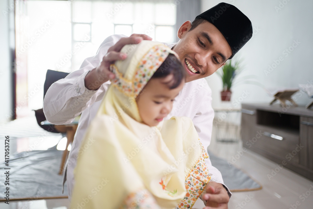 portrait of muslim father teaching her cute daughter how to pray at home