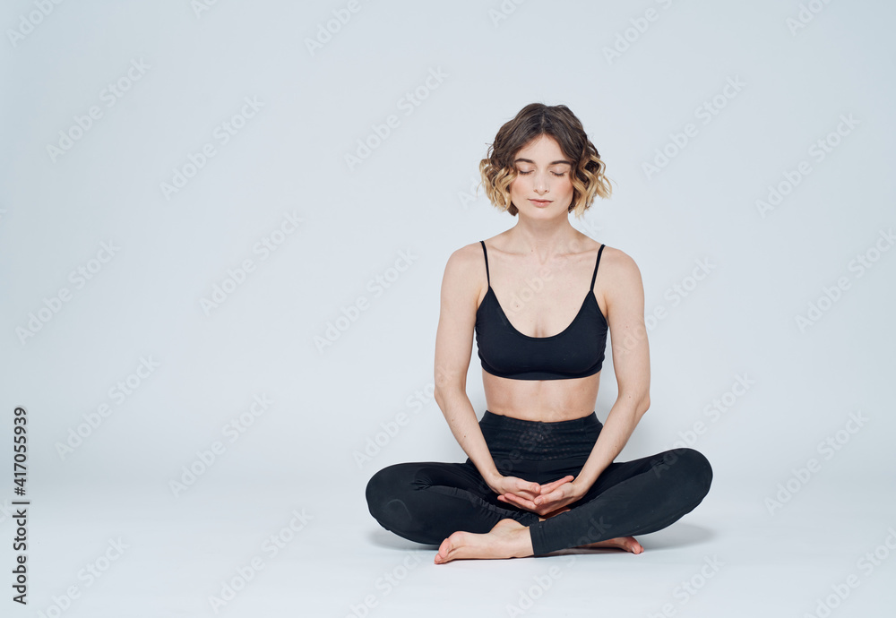 A woman is meditating on a light background with her legs crossed on the floor A woman is meditating on a light background with her legs crossed on the floor