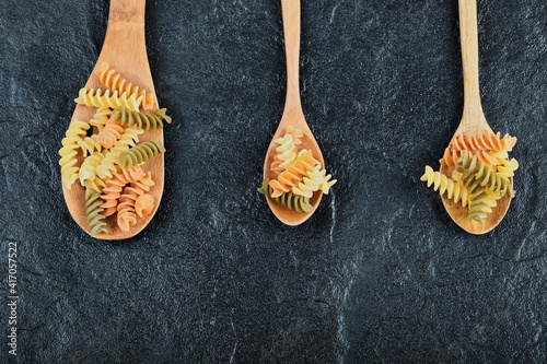 Various uncooked pasta on wooden spoons over dark background