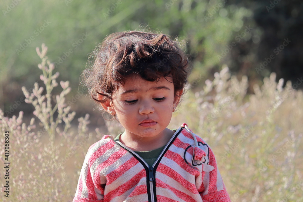 A beautiful little Indian child stands in the field and the natural blur background of white bushes in the back, A beautiful little Indian child stands in the field and the natural blur background of white bushes in the back,