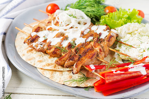 Grilled chicken kebab with pita, fresh vegetables on a white table. Grilled meat skewers, shish kebab on white background.