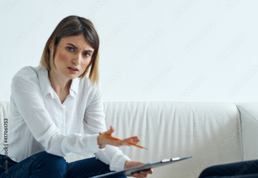 female psychologist with a folder of documents sits on the couch in a bright room female psychologist with a folder of documents sits on the couch in a bright room