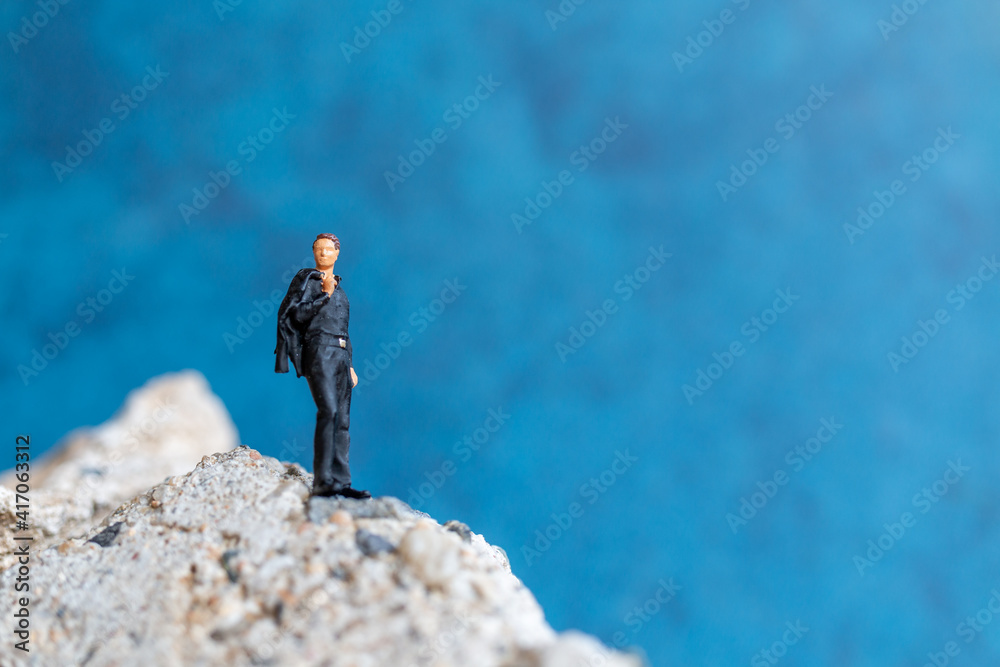 Miniature people Businessman standing on the rock with blue background