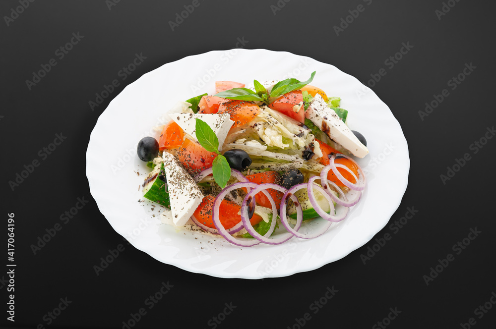 Greek salad on a white plate..Tomatoes, cucumbers, bell peppers, salad mix, feta cheese, olive oil. Dark background. Isolated. Close-up. Greek salad on a white plate..Tomatoes, cucumbers, bell peppers, salad mix, feta cheese, olive oil. Dark background. Isolated. Close-up.