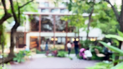 Abstract blurred footage people hanging out in green garden in front of building for title background. Blur outdoor hotel, cafe and restaurant with people surrounded by green tropical nature garden. photo