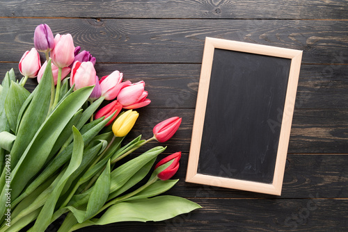 colorfull tulips with blank chalkboard over black wooden table background