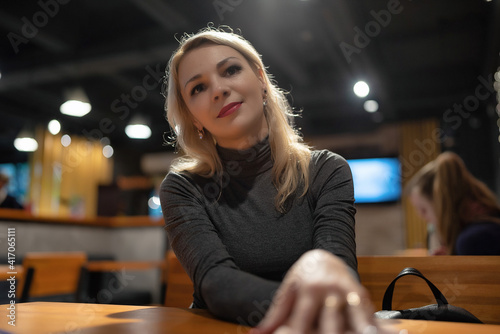 Young beautiful blonde girl drinks coffee in the evening in a cafe.