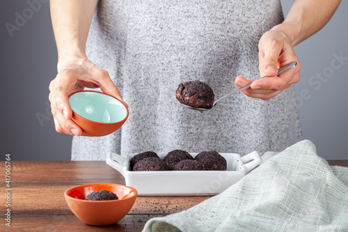 A woman is putting hashasli tatli (poppy seed covered cake balls) into serving bowls. This is a traditional dessert recipe from Turkey. Baked cacao cake balls are covered with poppy seeds. photo