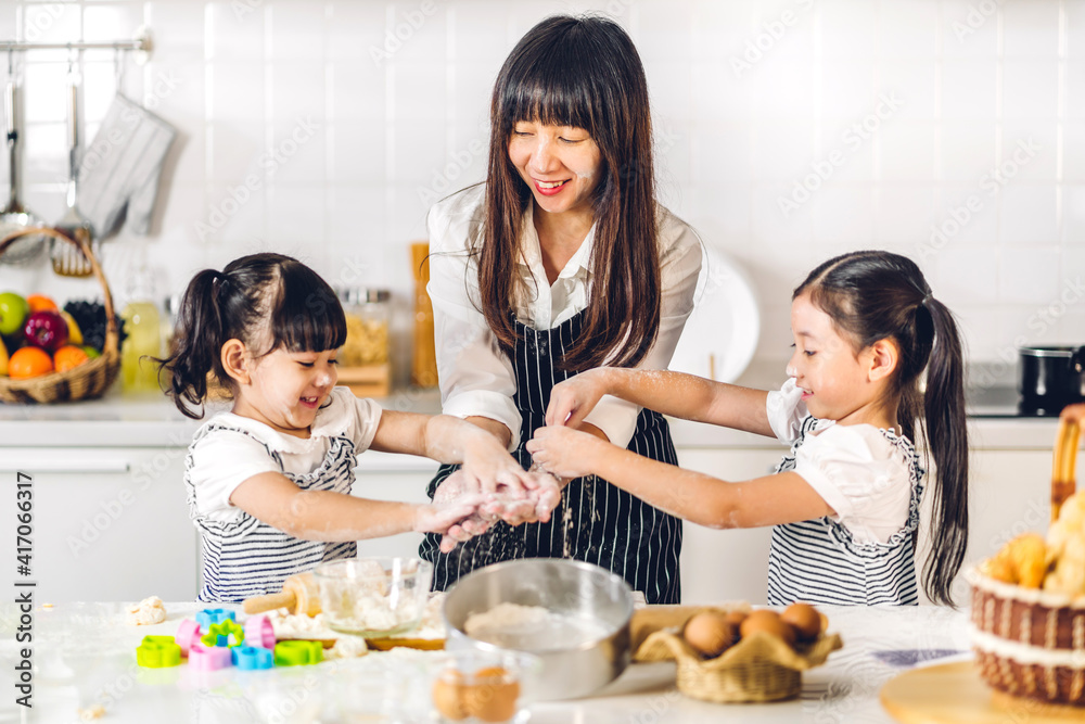 Portrait of enjoy happy love asian family mother and little asian girl daughter child having fun cooking together with baking cookies and cake ingredients on table in kitchen Portrait of enjoy happy love asian family mother and little asian girl daughter child having fun cooking together with baking cookies and cake ingredients on table in kitchen