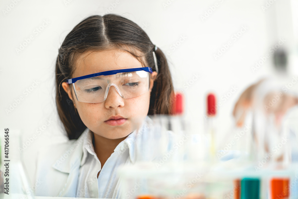 Cute little girl student child learning research and doing a chemical experiment while making analyzing and mixing liquid in glass at science class in school.Education and science concept Cute little girl student child learning research and doing a chemical experiment while making analyzing and mixing liquid in glass at science class in school.Education and science concept