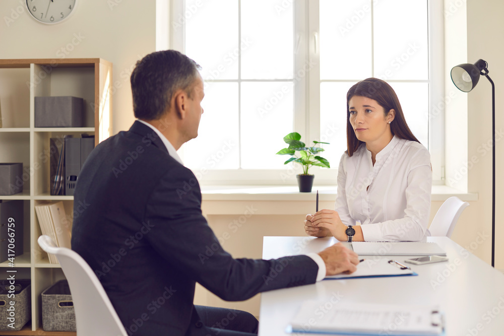 Fototapeta premium Young man and woman in formal wear sitting at desk and talking during business meeting in office. Executive listening to employee's report. Financial adviser helping customer answering her questions