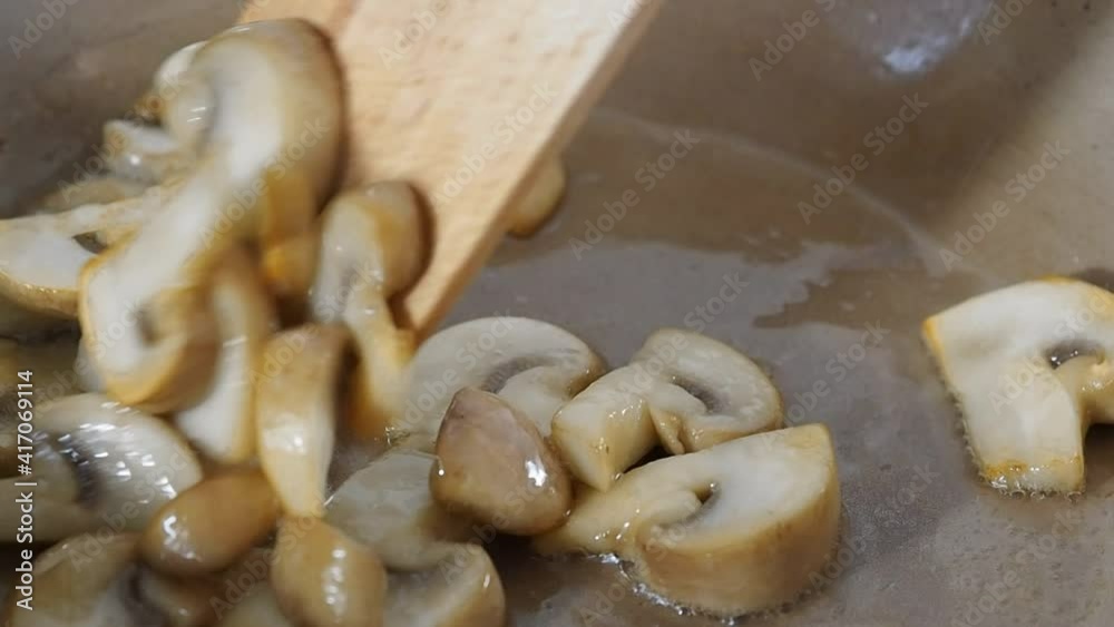 Sliced mushrooms champignons fried in oil in a frying pan. Close up. The cook stirs the mushrooms with a wooden spatula in a frying pan.
