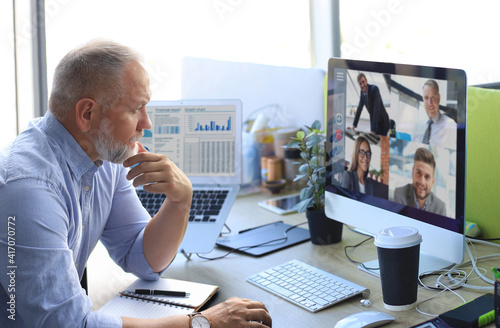 Mature businessman talking to his colleagues in video conference. Multiethnic business team working from office using computer PC, discussing financial report of their company