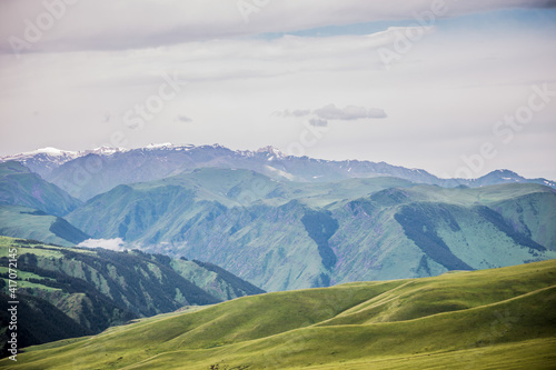 Endless steppe in the valley at the foot of the mountains, bathed in bright sunlight. Amazing view on  green mountains. mountain, covered with green trees, under a blue sky with clouds.