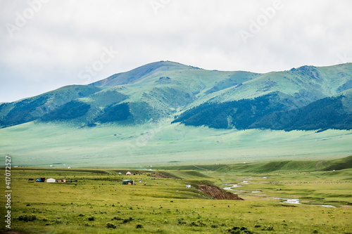 Endless steppe in the valley at the foot of the mountains, bathed in bright sunlight. Amazing view on  green mountains. mountain, covered with green trees, under a blue sky with clouds. © denis