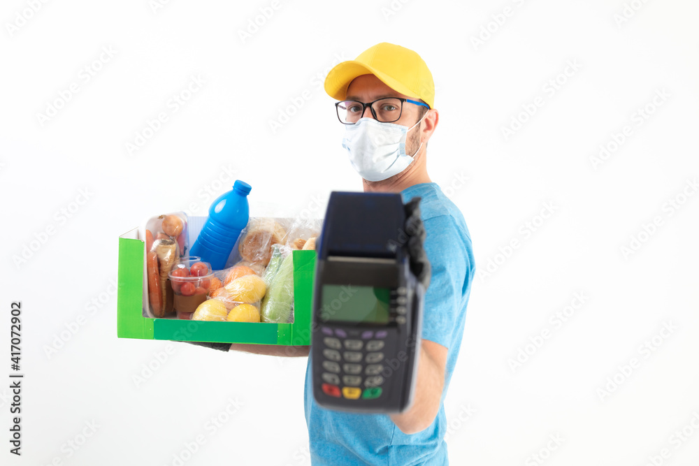 Delivery guy in front of a white wall with protective mask holding box with groceries and POS for contactless payment. Delivery guy in front of a white wall with protective mask holding box with groceries and POS for contactless payment.