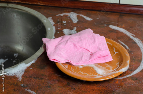 A pink viscose dishcloth and a brown plate on the kitchen table with foam.
