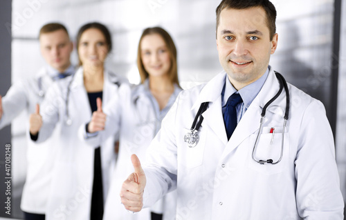 Group of professional doctors are standing as a team with thumbs up in a hospital office  ready to help their patients. Medical help  insurance in health care and medicine concept