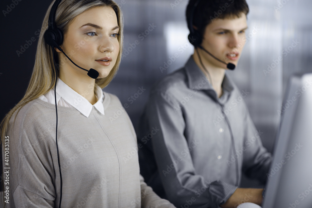 Diverse people group in call center. Blonde business woman talking by headset while sitting in modern office. Telemarketing and customer service concept Diverse people group in call center. Blonde business woman talking by headset while sitting in modern office. Telemarketing and customer service concept