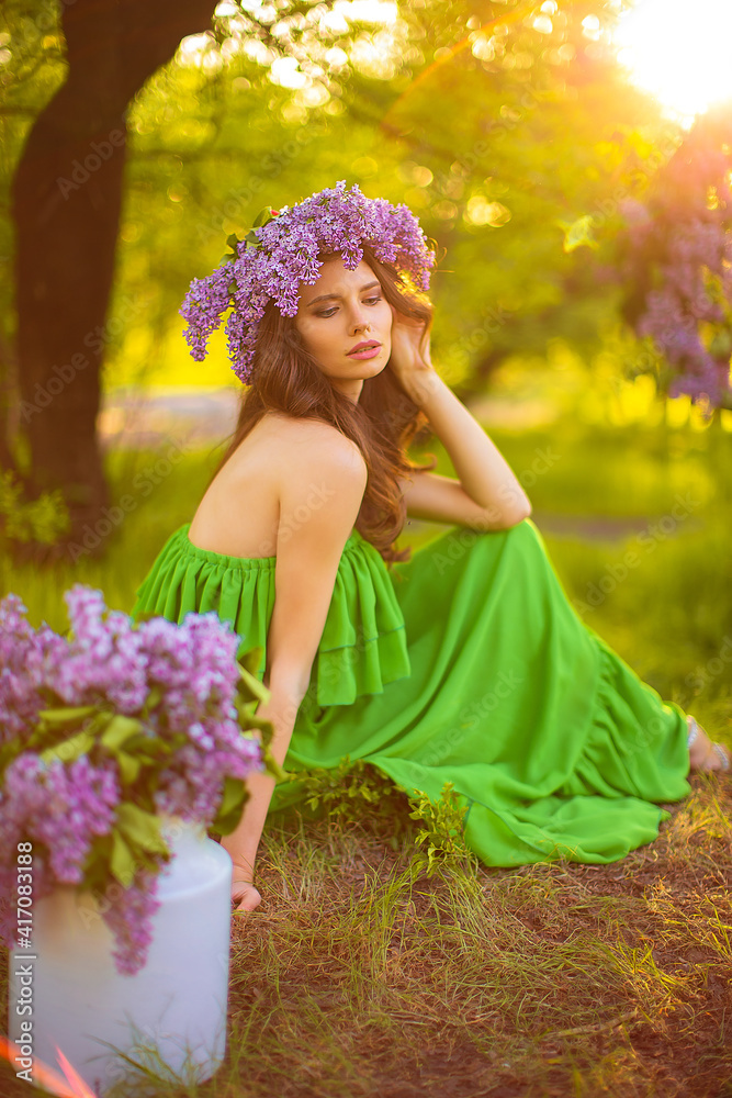 Fototapeta premium attractive woman in green dress posing near lilac flower decor.