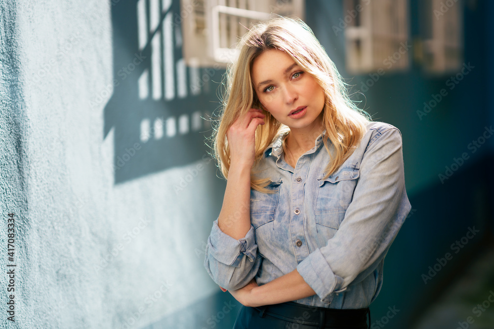 Blonde woman wearing denim shirt and black leather skirt standing in the street. Blonde woman wearing denim shirt and black leather skirt standing in the street.