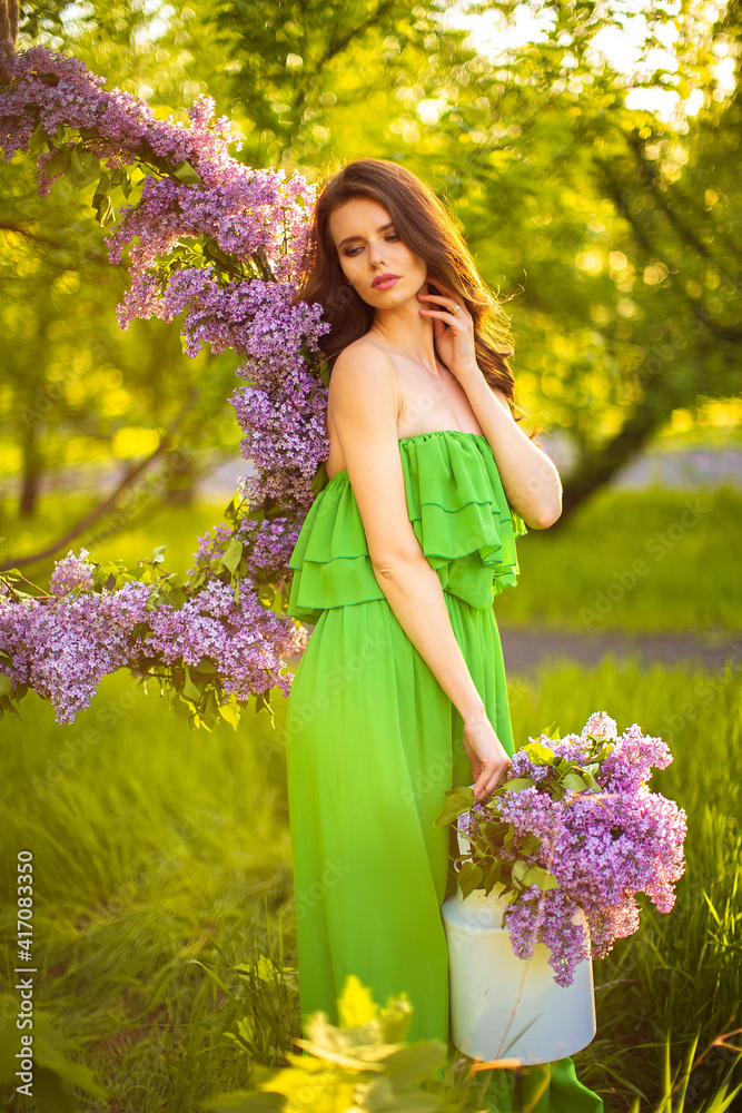 attractive woman in green dress posing near lilac flower decor. attractive woman in green dress posing near lilac flower decor.