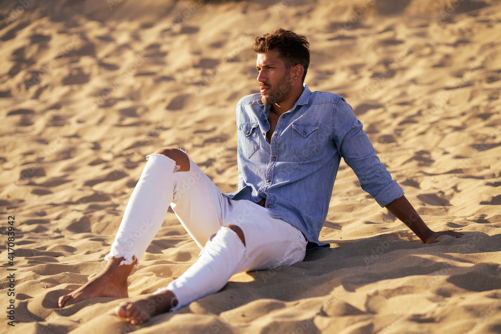 Attractive man sitting on the sand of the beach Attractive man sitting on the sand of the beach