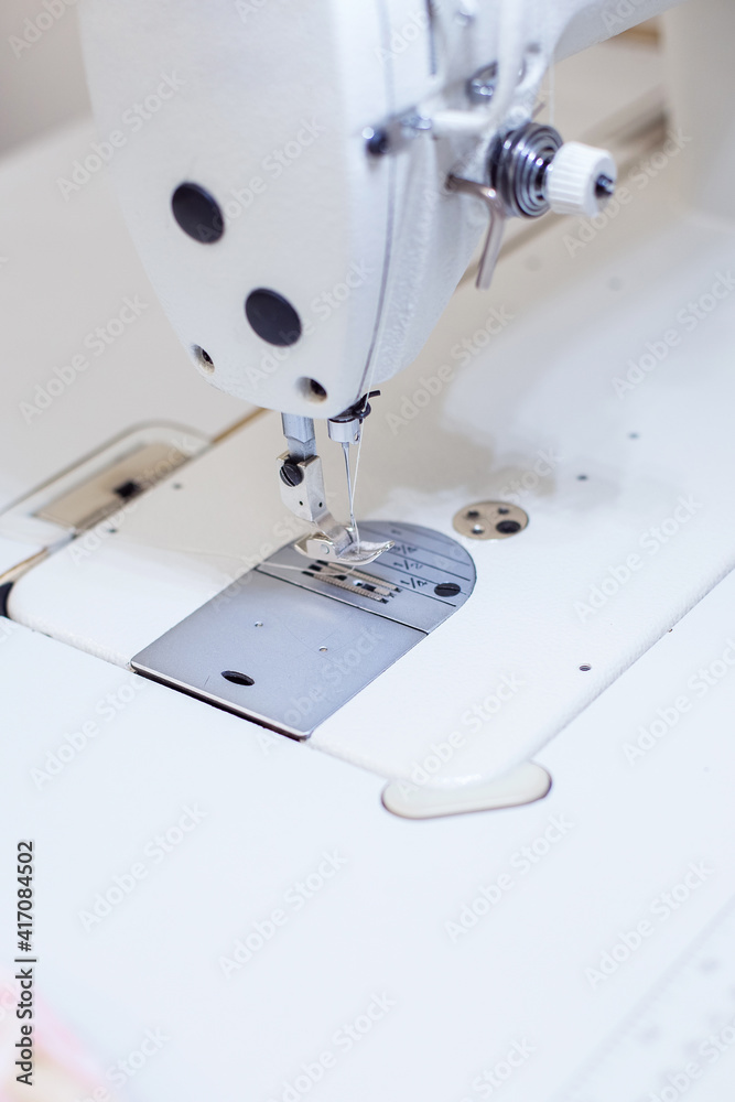 a female seamstress inserts a thread into a needle on a sewing machine. The dressmaker works on a sewing machine. A tailor sews clothes at his workplace. Hobby sewing as a small business concept