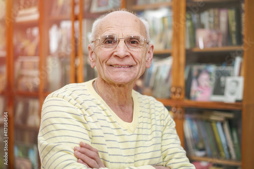 Portrait of cheerful kindly gray haired senior man in glasses against bookcase.