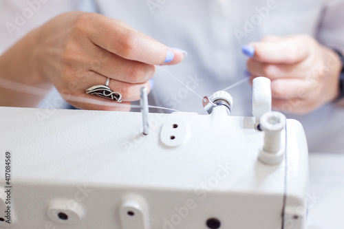 a female seamstress inserts a thread into a needle on a sewing machine. The dressmaker works on a sewing machine. A tailor sews clothes at his workplace. Hobby sewing as a small business concept