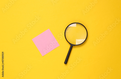 Magnifier and memo paper on a yellow background. Search concept